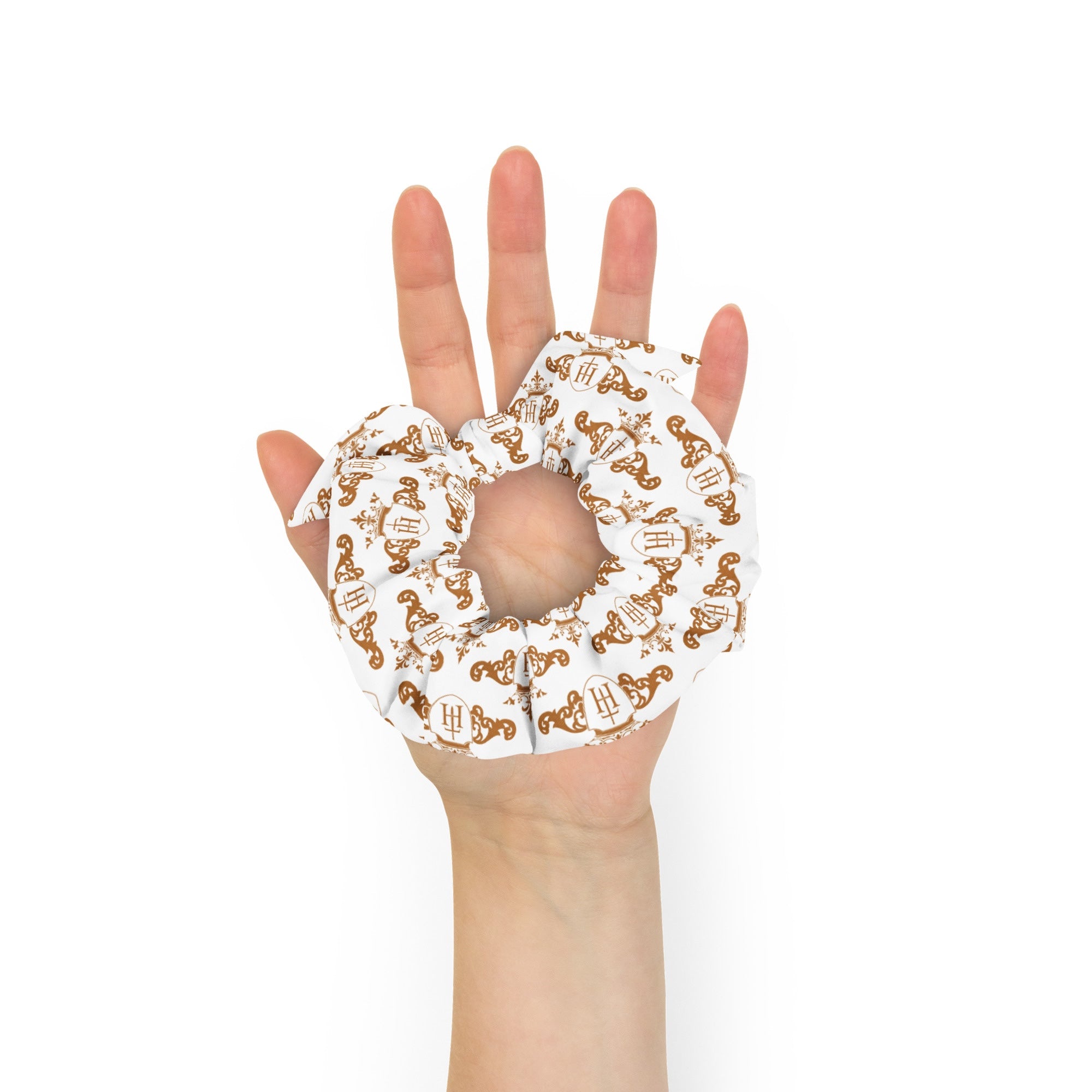 Hand holding a decorative scrunchie with intricate gold crest patterns on a white background
