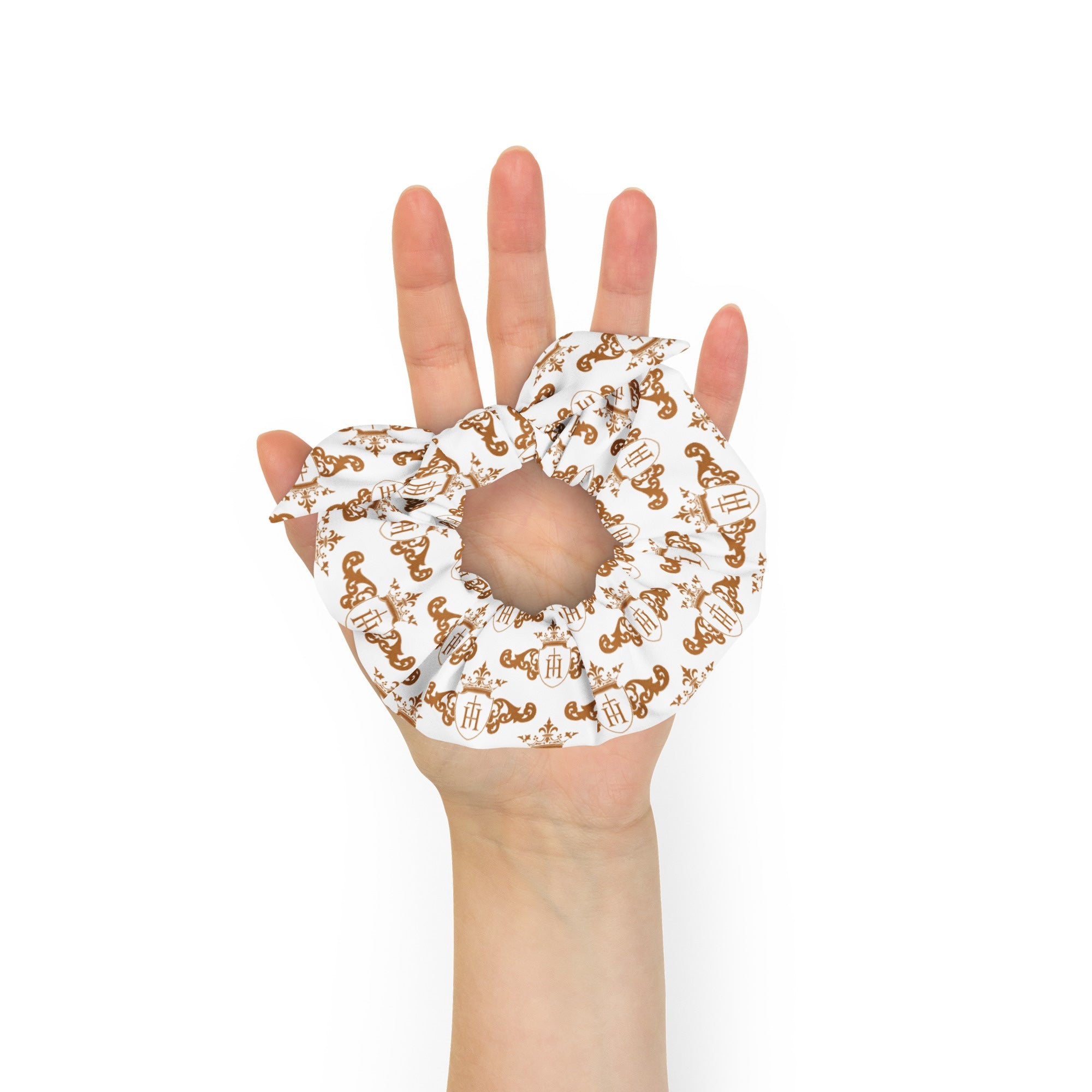 Hand wearing a white scrunchie with gold crest patterns on a white background