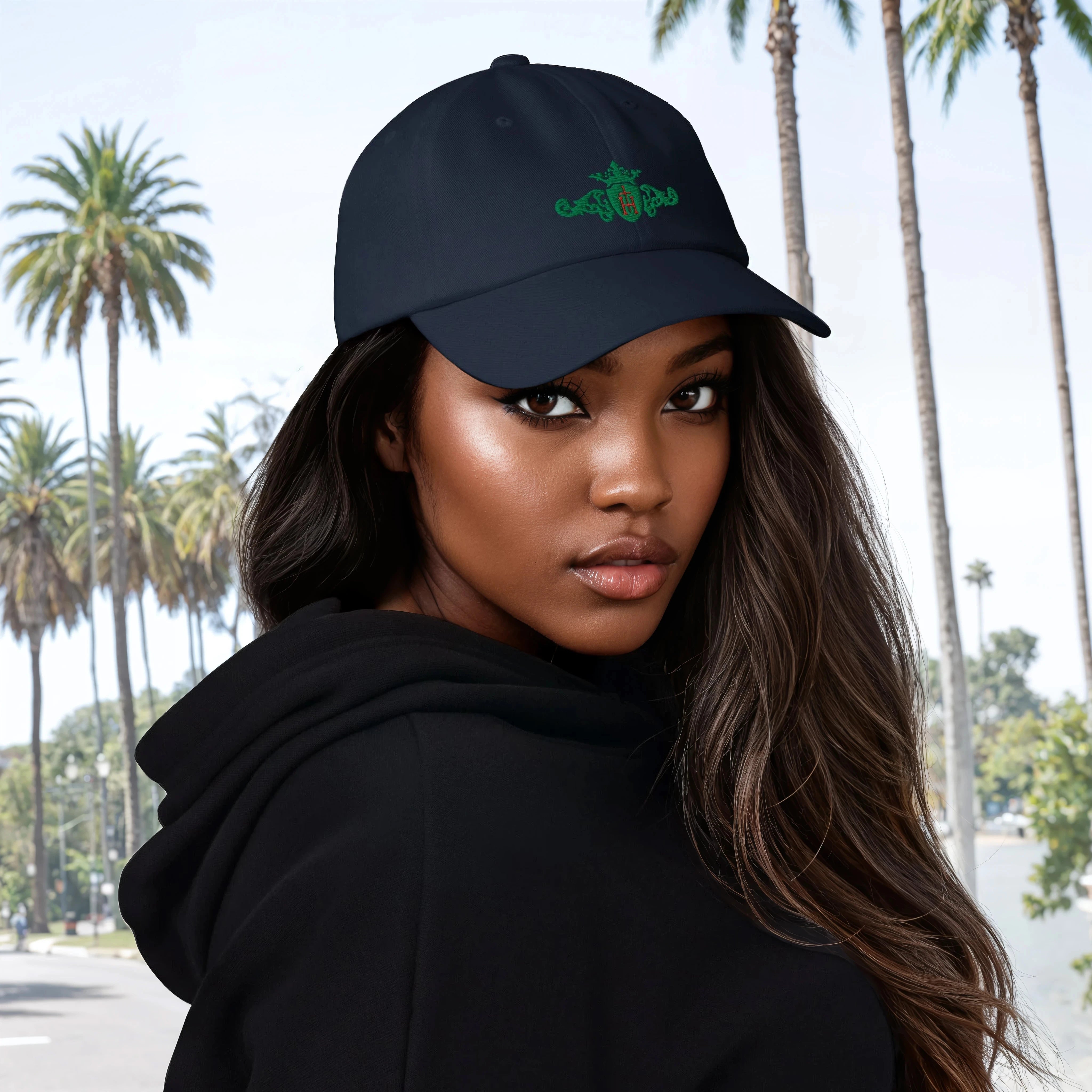 Woman wearing a black cap with a unique kelly-green crest with a red center in front of a palm tree background