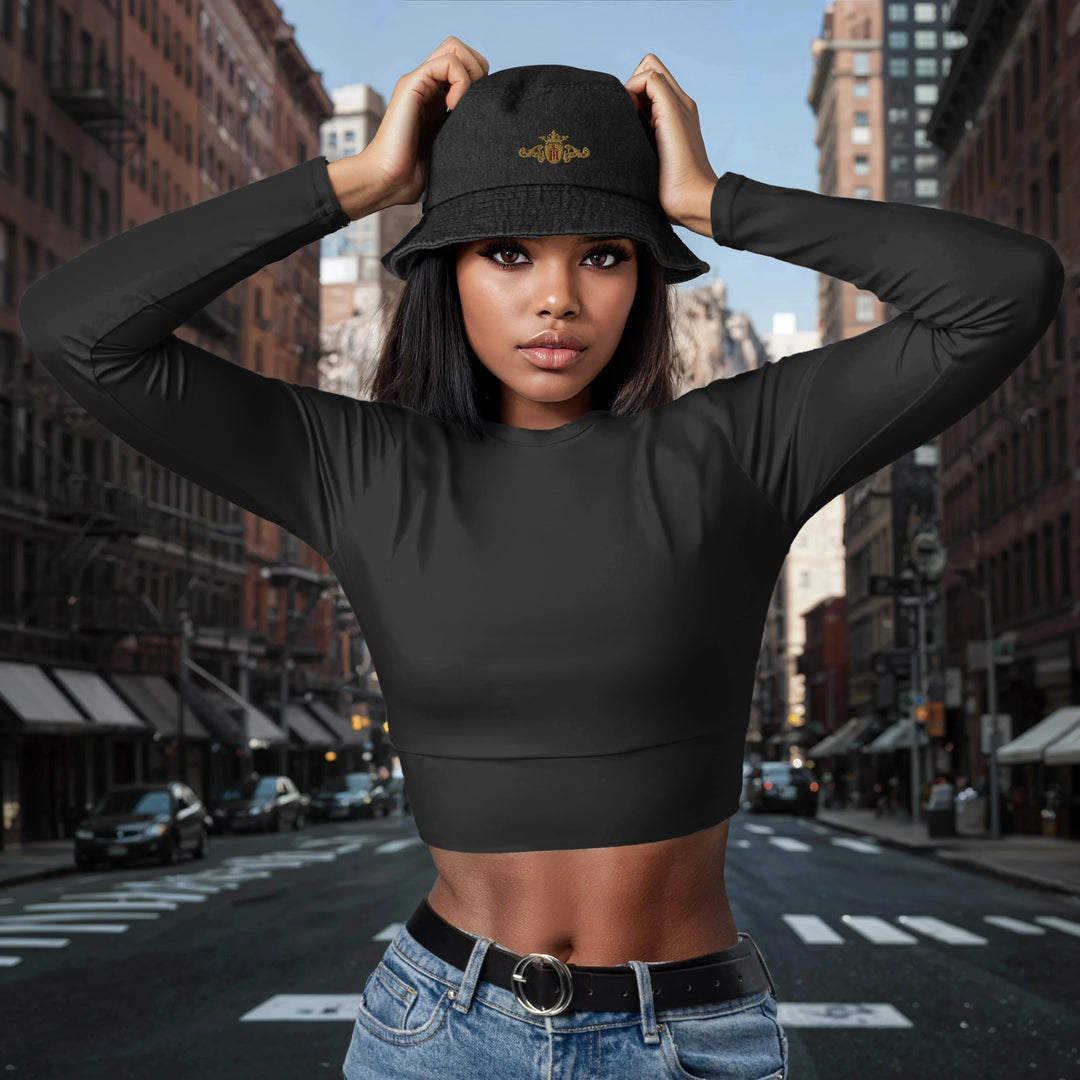 Woman wearing a black crop top and a black denim bucket hat with a gold crest with a maroon center on a city street