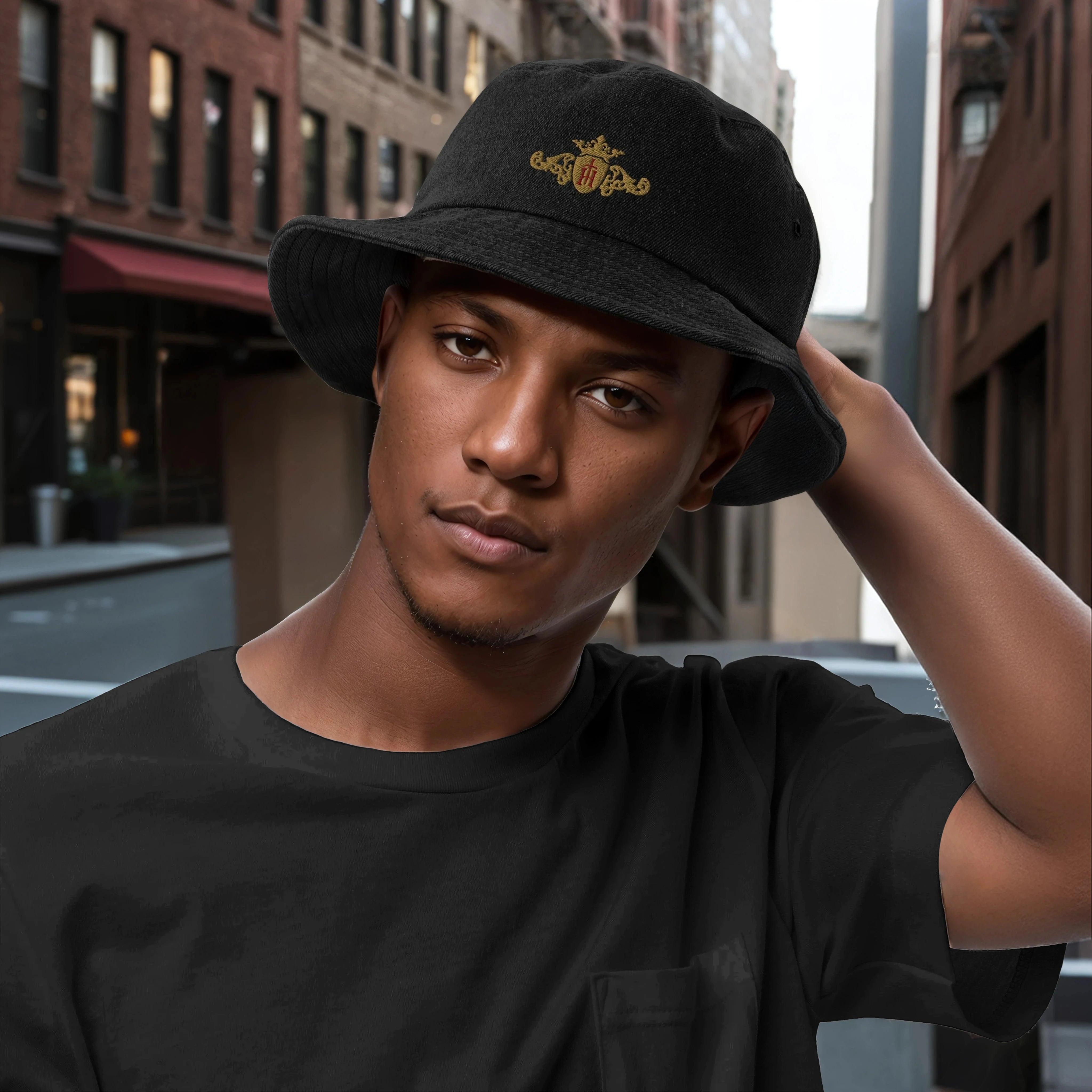 Man wearing a black denim bucket hat with a unique gold crest with a maroon center in an urban setting