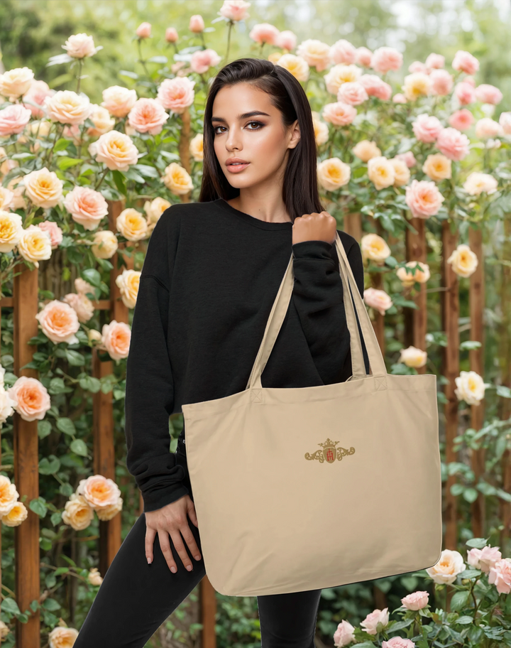 Woman holding a beige tote bag with a gold and red crest in front of a floral background