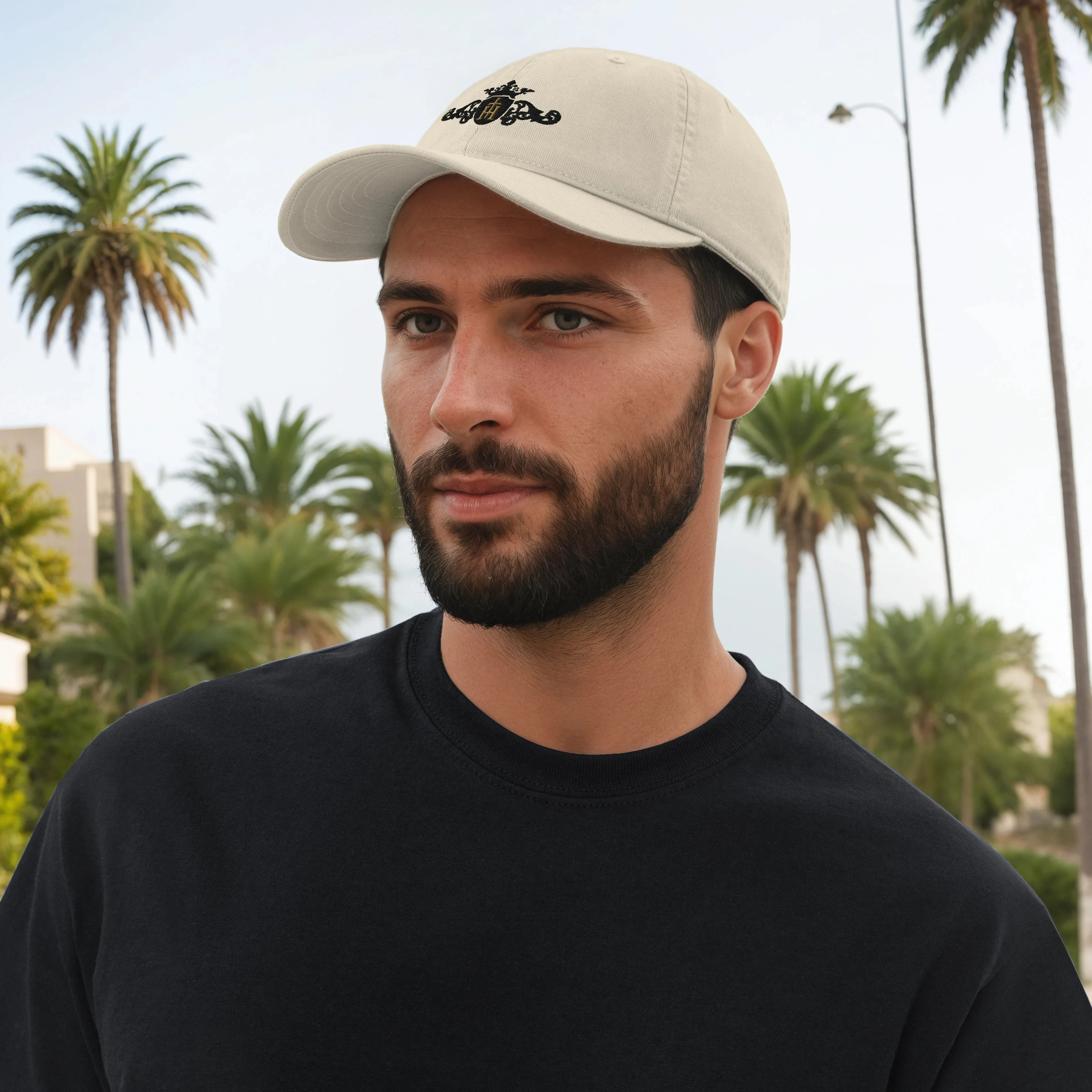 Man wearing a beige cap with a logo and black shirt in front of palm trees