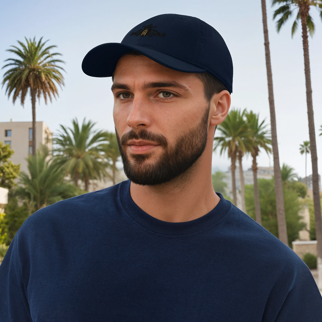 Man wearing a navy cap with a black and gold crest and a sweatshirt with palm trees in the background